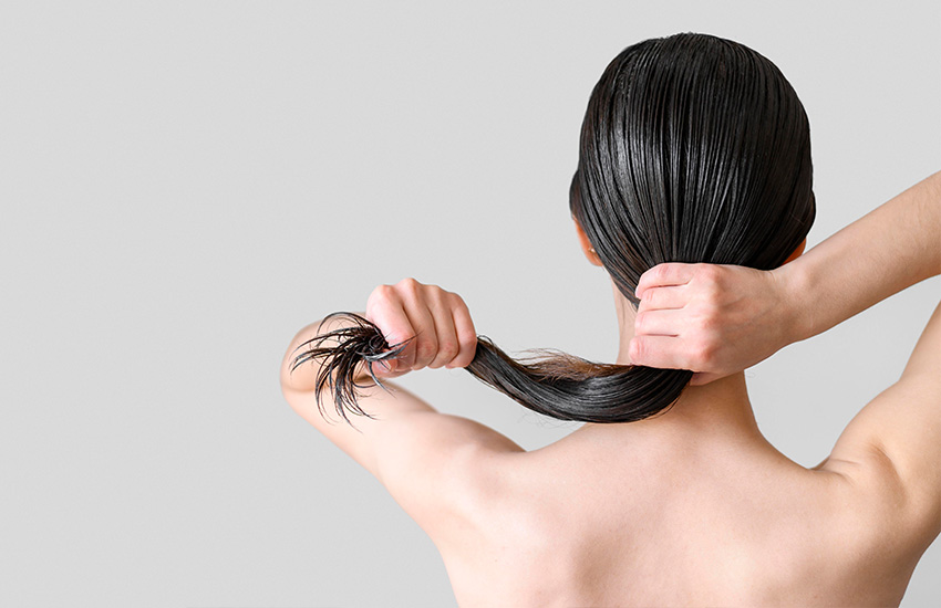 Mujer de espaldas sostiene su cabello húmedo con ambas manos formando una coleta